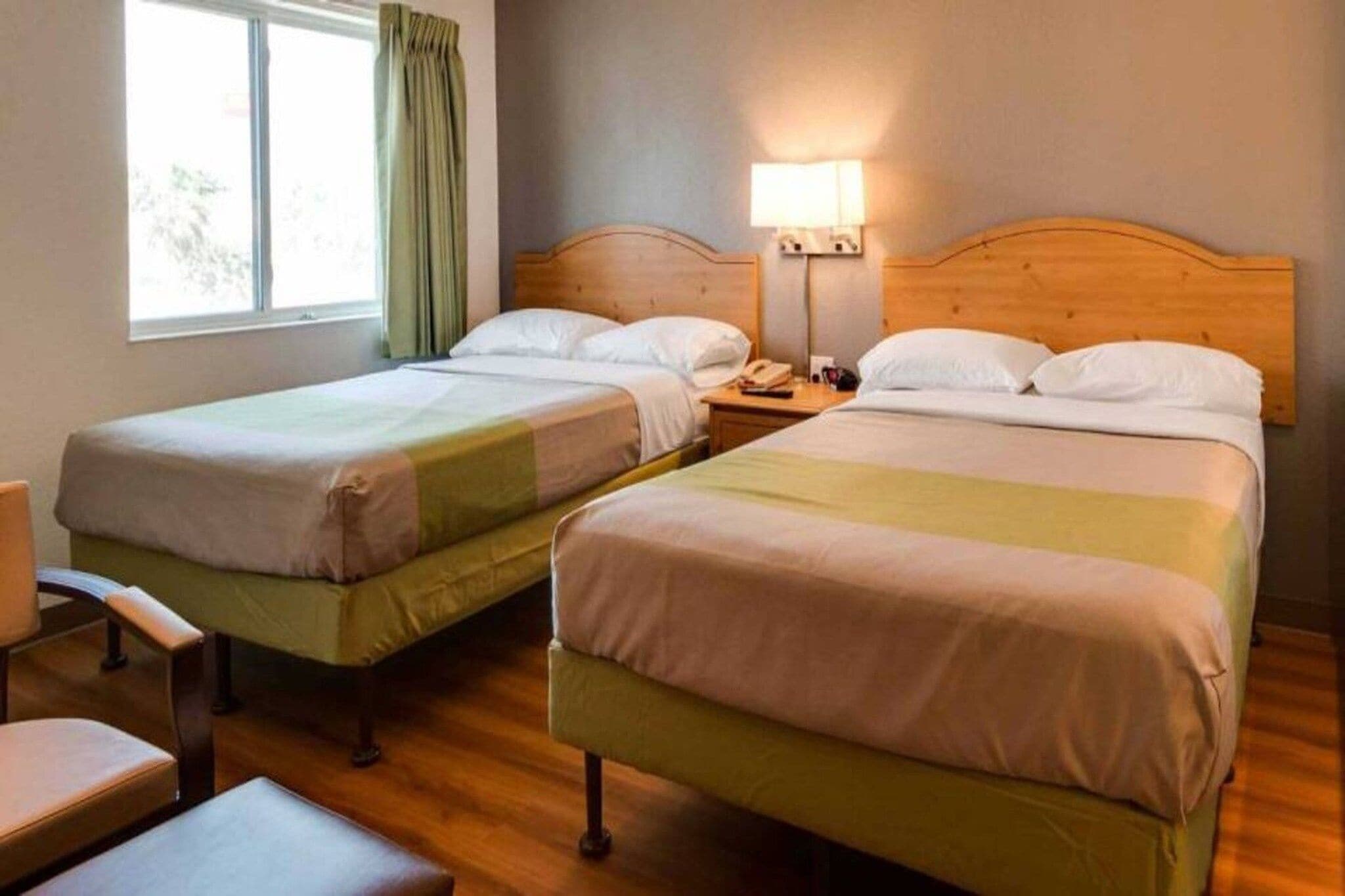 Hotellihuone, jossa on kaksi erillistä sänkyä, puinen pääty, yöpöytä lampun kanssa ja tuoli.