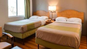 Hotellihuone, jossa on kaksi erillistä sänkyä, puinen pääty, yöpöytä lampun kanssa ja tuoli.