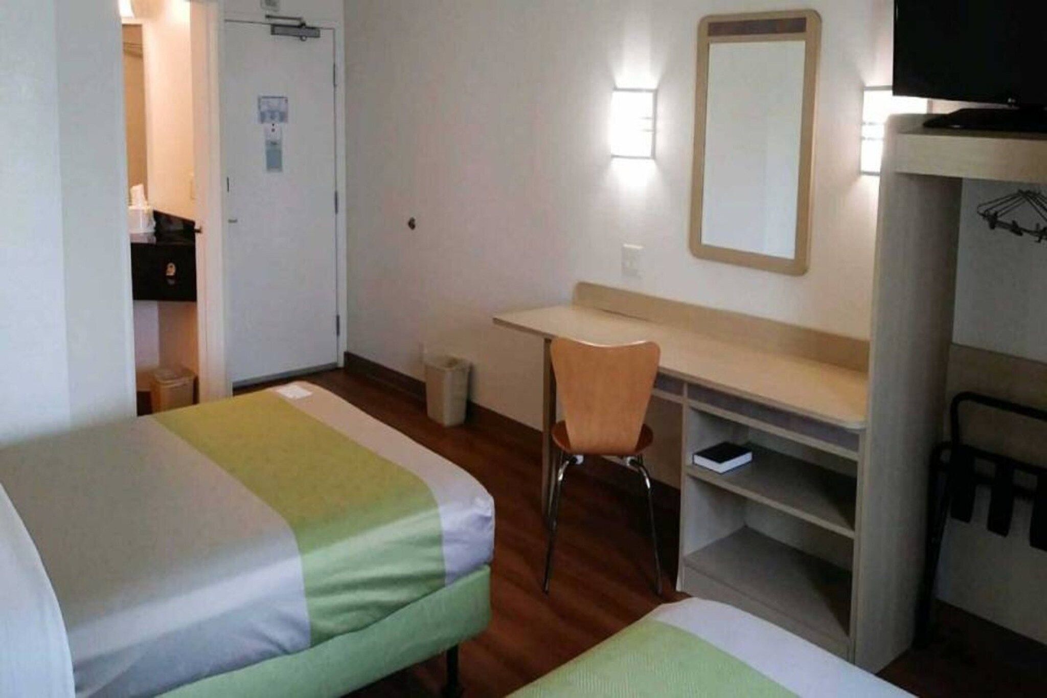 A hotel room with two beds, a desk, a chair, a television, and a mirror.