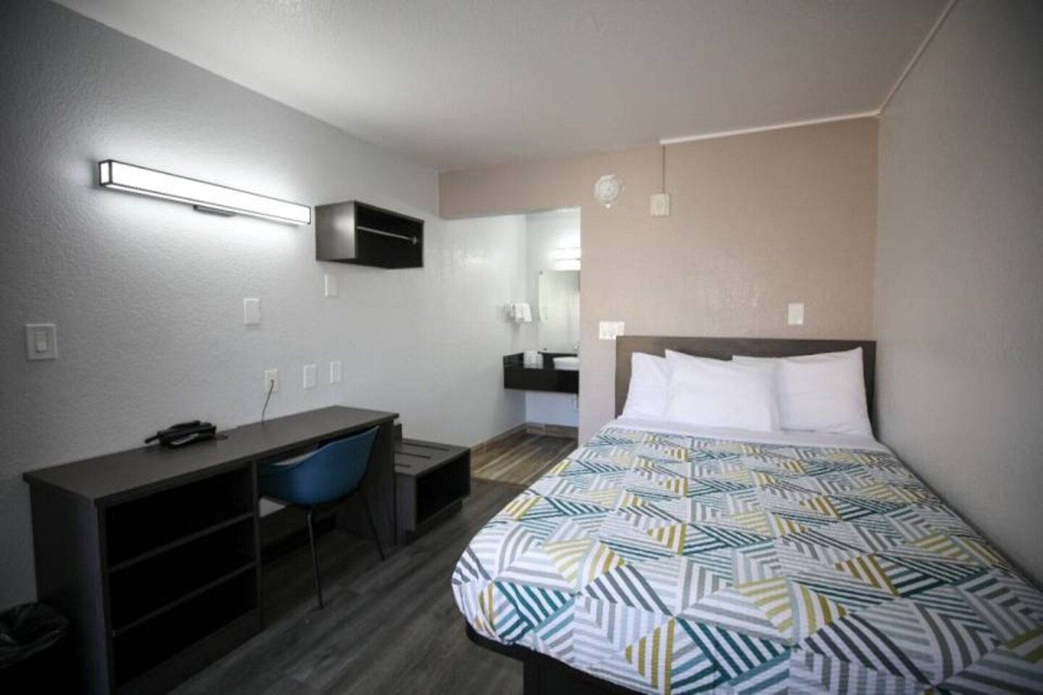 Een hotelkamer met een bed, een bureau, een stoel, een spiegel en een aan de muur bevestigde televisie.