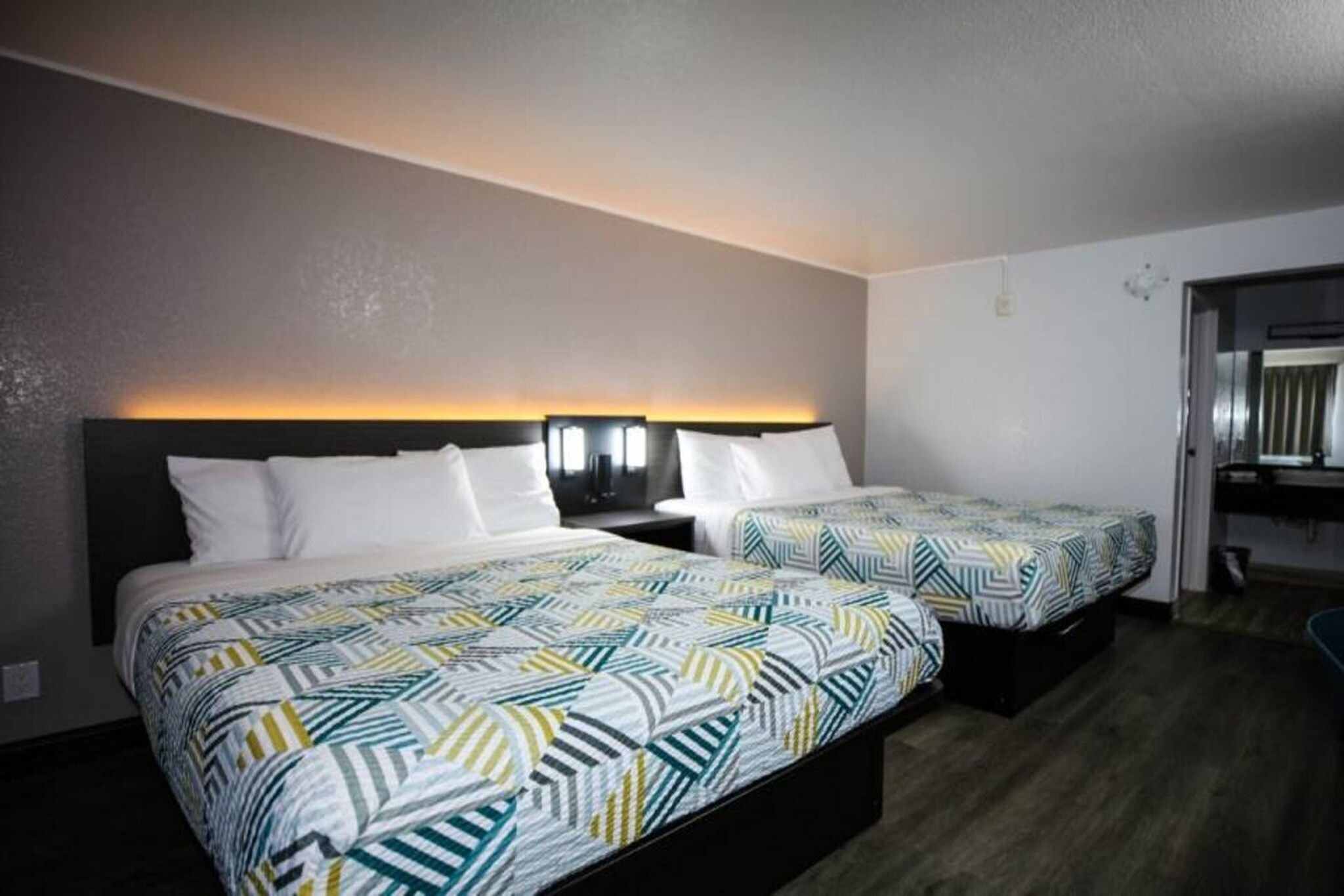 Une chambre d’hôtel avec deux lits, chacun recouvert d’une couvre-lit à motifs, une table de chevet avec une lampe et un luminaire fixé au mur.