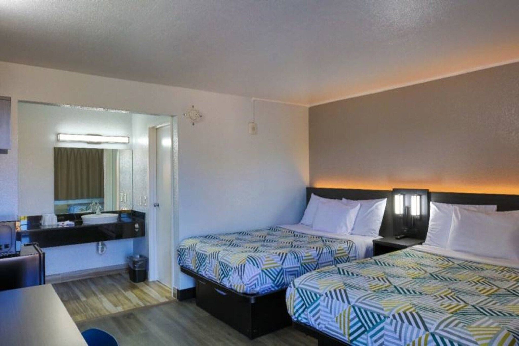 Una habitación de hotel con dos camas, un escritorio, un espejo y un baño pequeño.