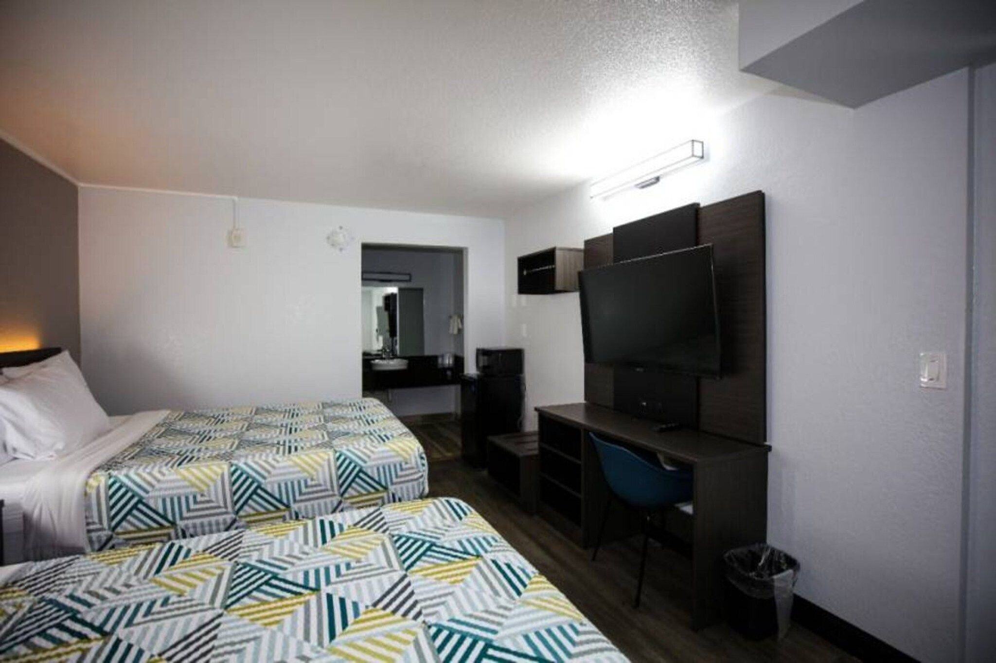 Une chambre d’hôtel avec deux lits, un bureau, une chaise, une télévision et une poubelle.