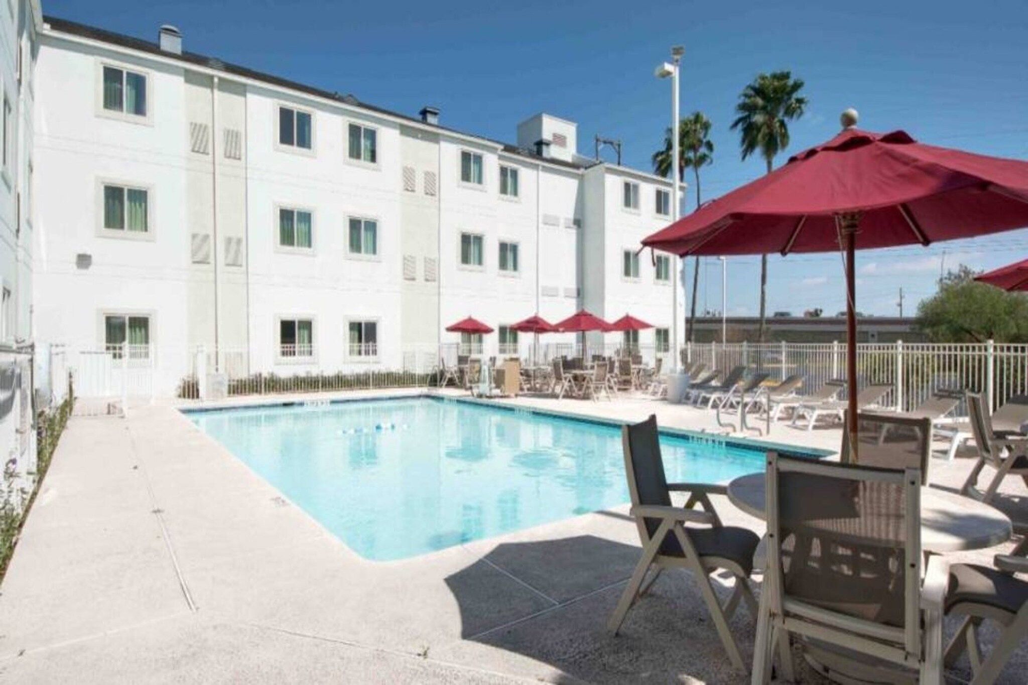 Ett poolområde vid hotellet med solstolar och parasoller, omgivet av en vit byggnad med många fönster.