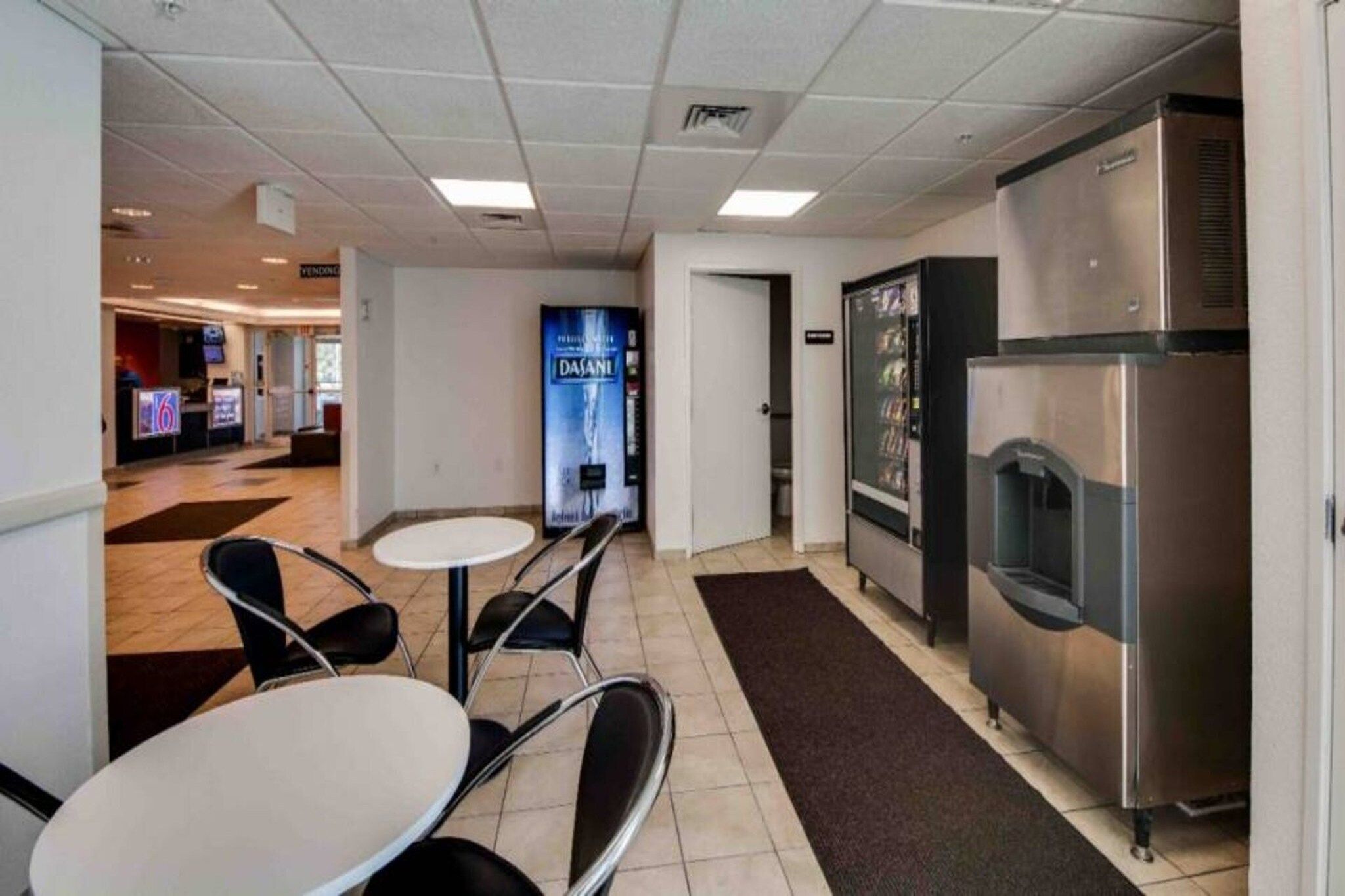 A hotel lobby with a reception desk, a vending machine, and a refrigerator.