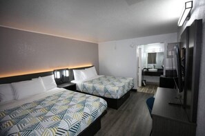 A hotel room with two beds, a desk, a mirror, and a small bathroom. - 2 Full Beds | Non-Smoking (Brownsville)