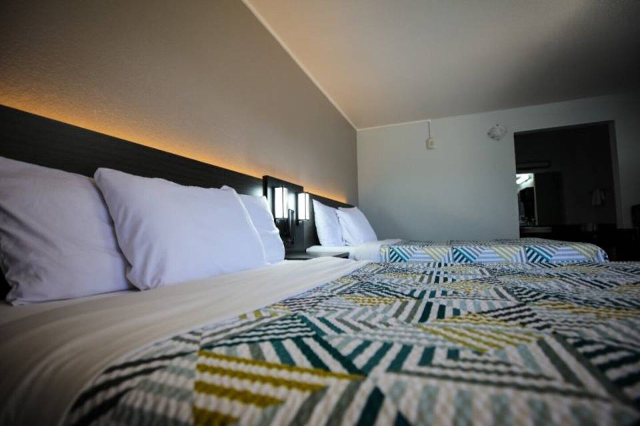 Et hotelværelse med to senge, et mønstret sengetæppe og en sengegavl med indbygget belysning.