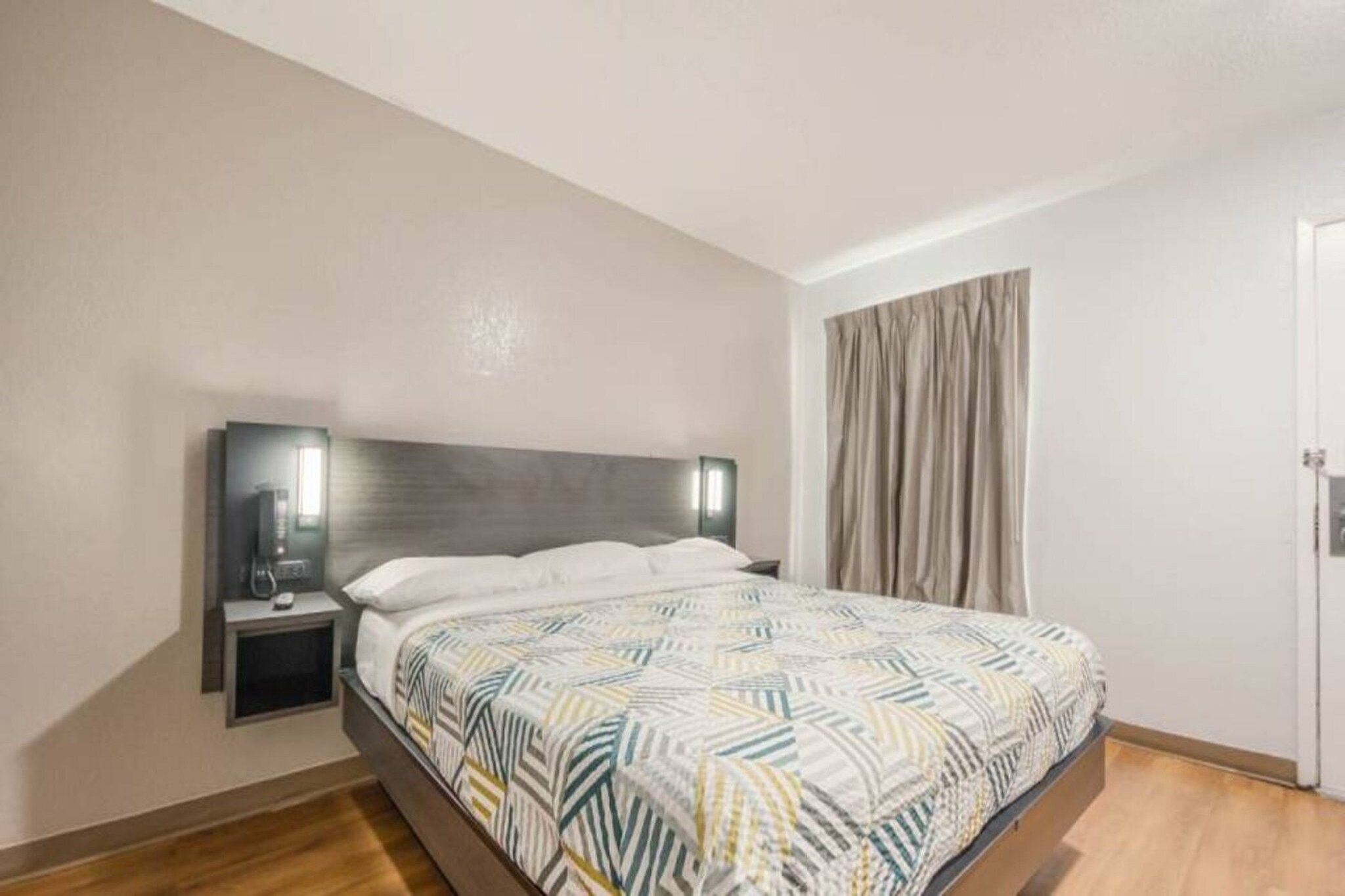 Une chambre à coucher avec un lit, des tables de chevet, une commode, une fenêtre avec des rideaux et une porte.