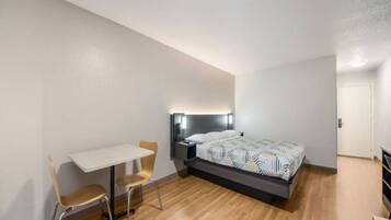 A bedroom with a bed, bedside table, chair, and a desk.
