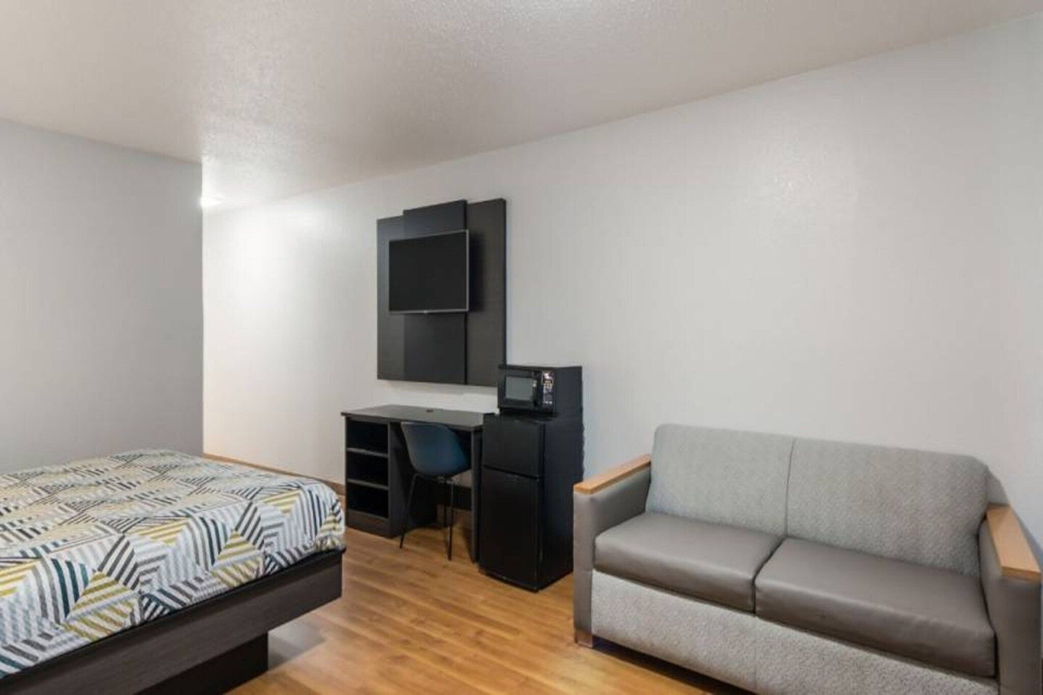 Habitación pequeña con cama, escritorio, silla y sofá.
