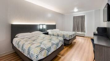 A hotel room with two beds, a desk, and a television.