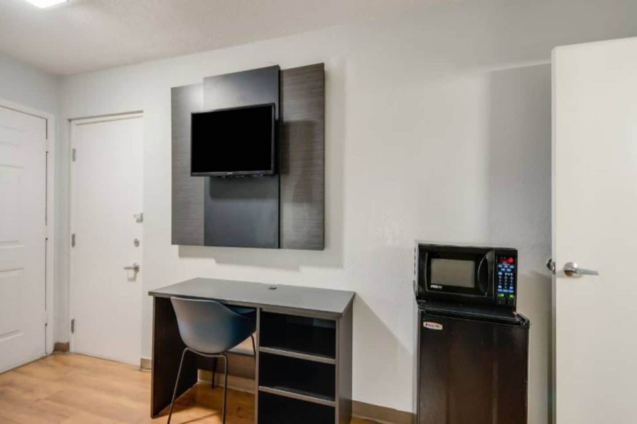 Ein Zimmer mit flachbildfernseher an der Wand, einem Schreibtisch mit Stuhl und einer Mikrowelle.