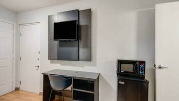 Ein Zimmer mit flachbildfernseher an der Wand, einem Schreibtisch mit Stuhl und einer Mikrowelle.