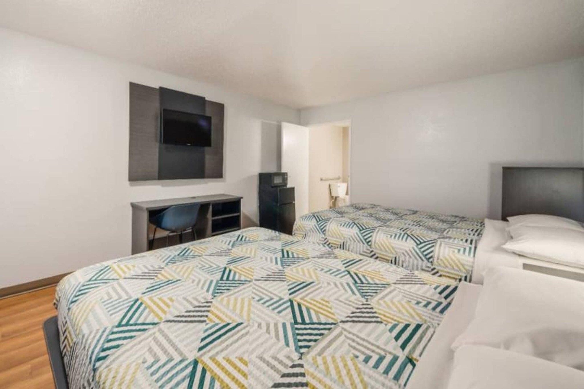 Habitación de hotel con dos camas, un escritorio, una silla, un televisor y un microondas.
