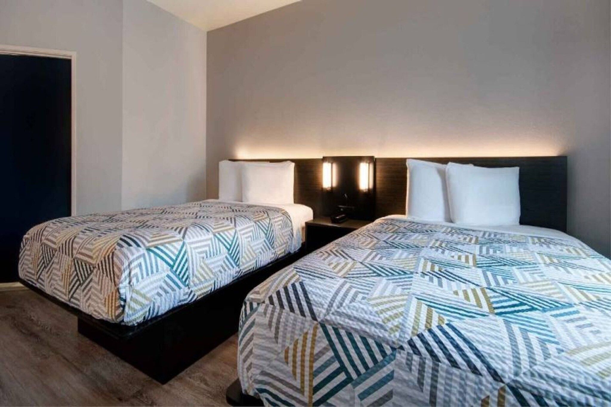 Habitación de hotel con dos camas, cada una con una colcha estampada, lámparas de noche y cabeceros oscuros.