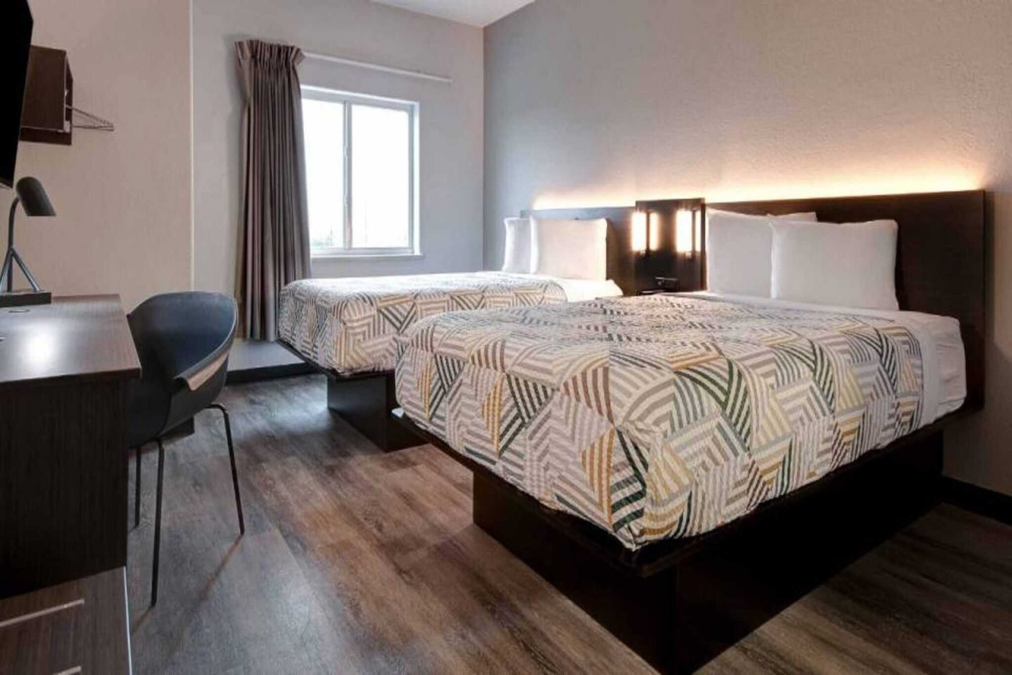 A hotel room with two beds, a desk, and a chair.