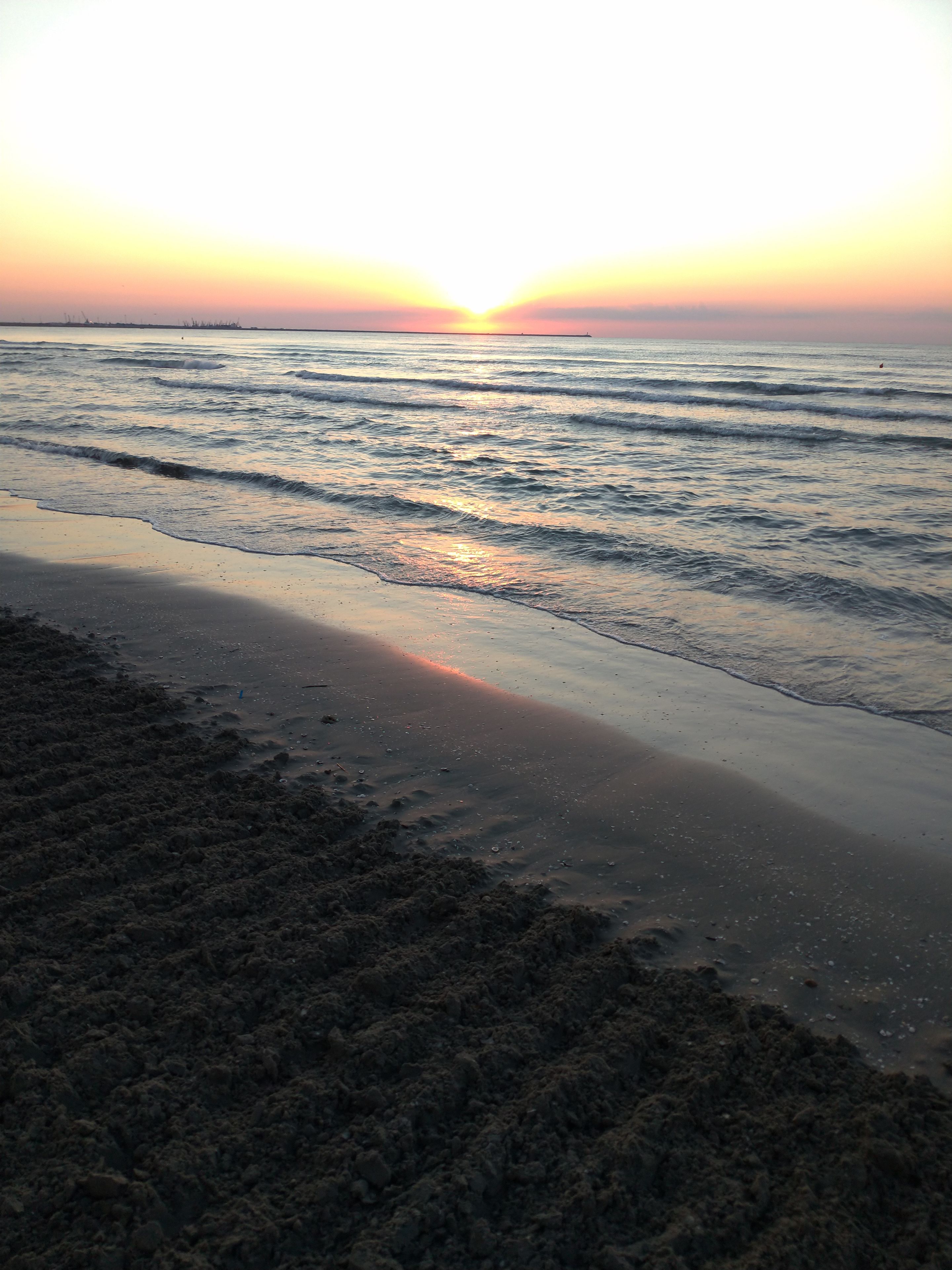 A beach with waves, a sunset, and a distant horizon.