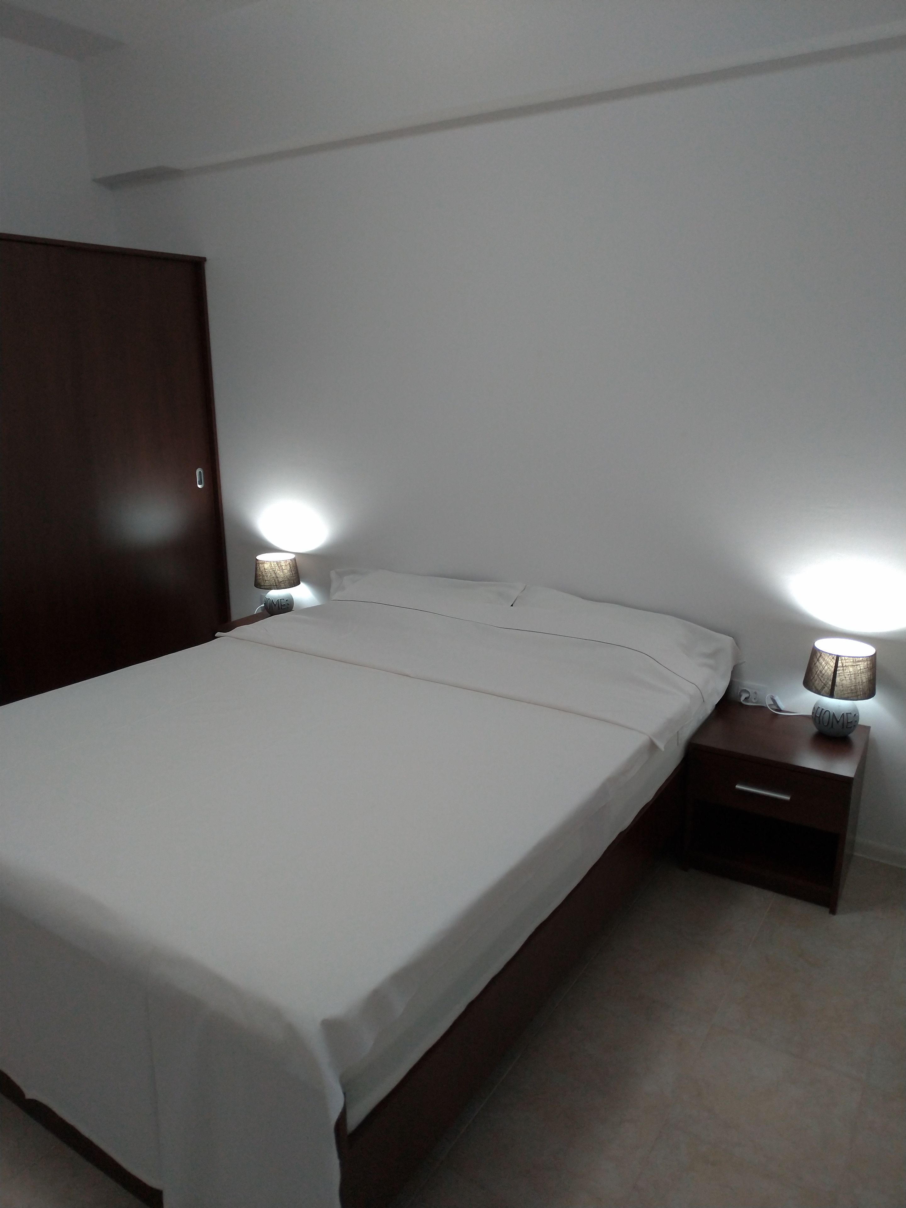 A bedroom with a large bed, a wooden wardrobe, and two bedside lamps.