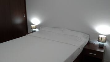 A bedroom with a large bed, a wooden wardrobe, and two bedside lamps.