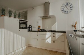 A modern kitchen with white cabinetry, a stainless steel sink, a vintage clock, and a coffee maker. - Luxury penthouse Shrimp in Egmond aan Zee for 5 guests, with 3 bedrooms, two levels and panoramic sea views. (Egmond aan Zee)