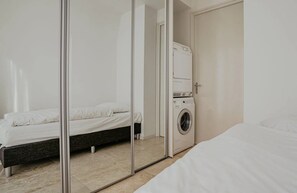 A bedroom with a bed, a washing machine, and a mirror reflecting the room. - Luxury penthouse Shrimp in Egmond aan Zee for 5 guests, with 3 bedrooms, two levels and panoramic sea views. (Egmond aan Zee)