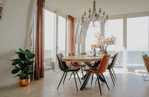 A dining area with a table and chairs, a chandelier, and a view of the sea. - Luxury penthouse Shrimp in Egmond aan Zee for 5 guests, with 3 bedrooms, two levels and panoramic sea views. (Egmond aan Zee)