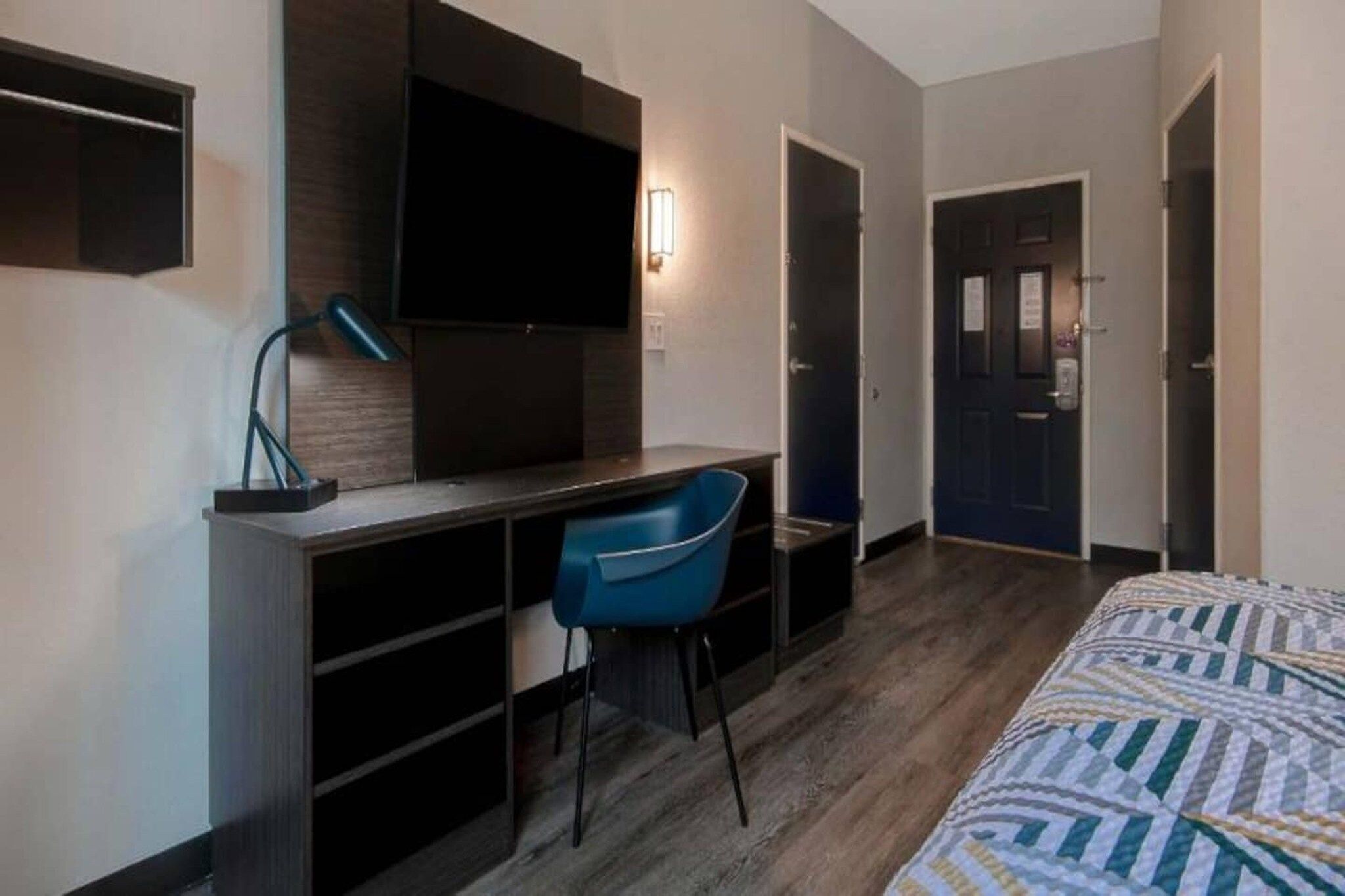 A hotel room with a bed, a desk with a chair, a TV, and a door.