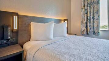 Een hotelkamer met een bed, nachtkastje, lamp en gordijnen.