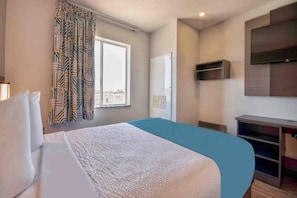 Habitación de hotel con cama, ventana con cortinas, televisión montada en la pared y escritorio con silla.