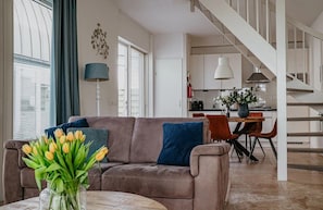 Una sala moderna con un sofá, una mesa de centro con un florero de tulipanes y una escalera que sube a un nivel superior.