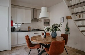 A modern kitchen with white cabinets, a wooden dining table, and a hanging light fixture. - Dune apartment Flat Fish in Egmond aan Zee for 3 guests, with a sun terrace, sea views and direct beach access. (Egmond aan Zee)