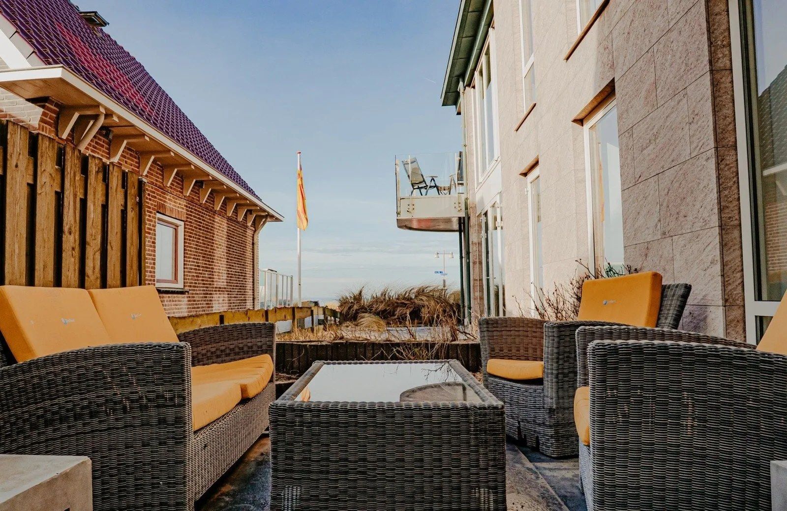 Un espace patio aménagé avec des meubles en osier et un mât pour drapeau.