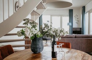 A modern living room with a round wooden table, a vase with flowers, a wine bottle, and a television in the background. - Dune apartment Flat Fish in Egmond aan Zee for 3 guests, with a sun terrace, sea views and direct beach access. (Egmond aan Zee)