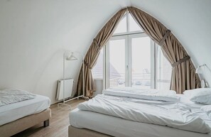 A bedroom with a large window, a radiator, a bedside table, and a lamp. - Dune apartment Flat Fish in Egmond aan Zee for 3 guests, with a sun terrace, sea views and direct beach access. (Egmond aan Zee)