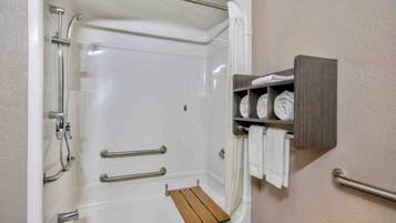 A bathroom with a shower, grab bars, and a shelf with towels.