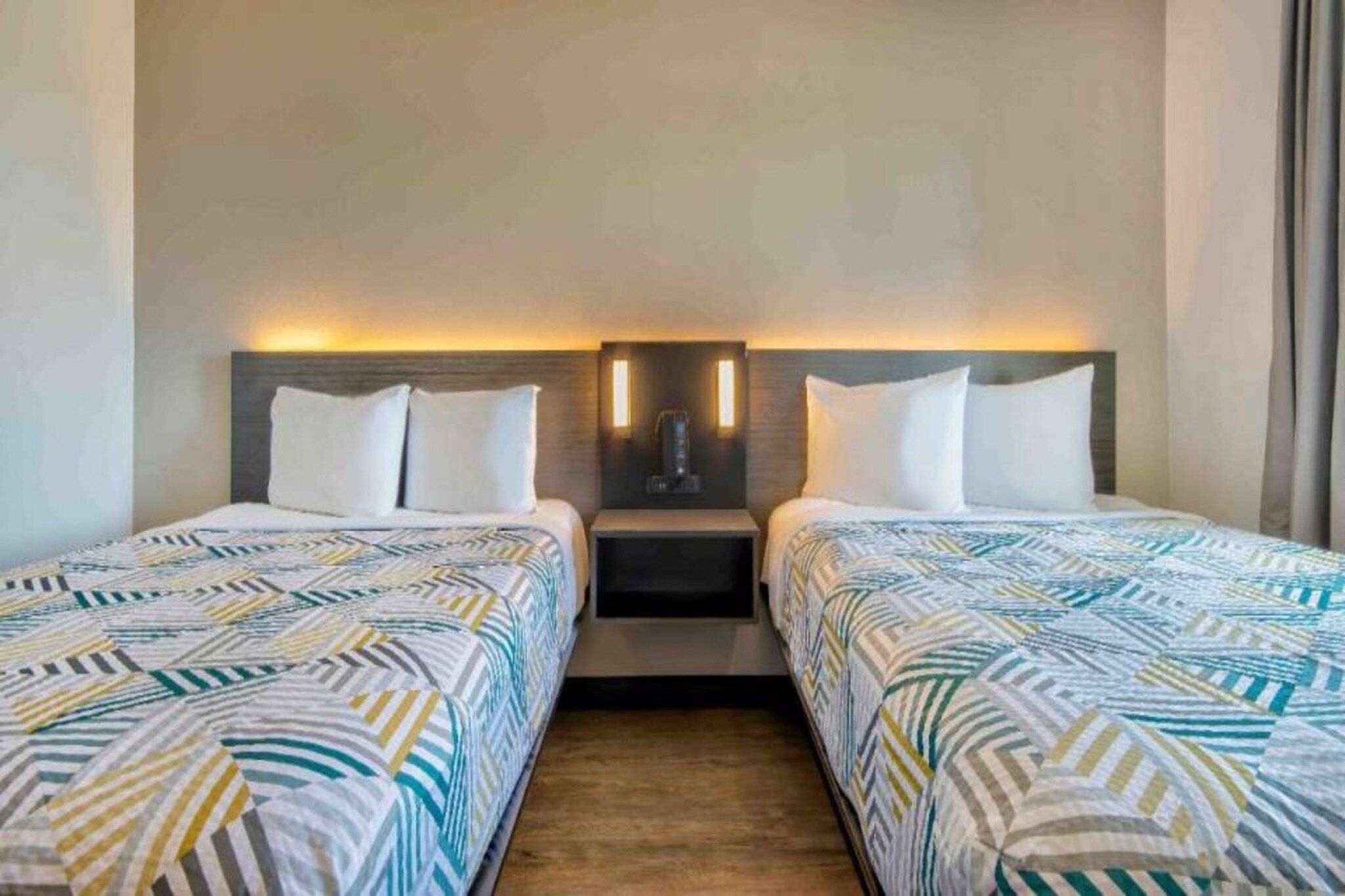 A hotel room with two beds, a nightstand, and a wall-mounted light fixture.
