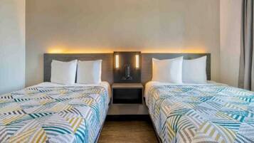 A hotel room with two beds, a nightstand, and a wall-mounted light fixture.