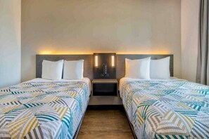 Habitación de hotel con dos camas, una mesita de noche y un aplique de pared.