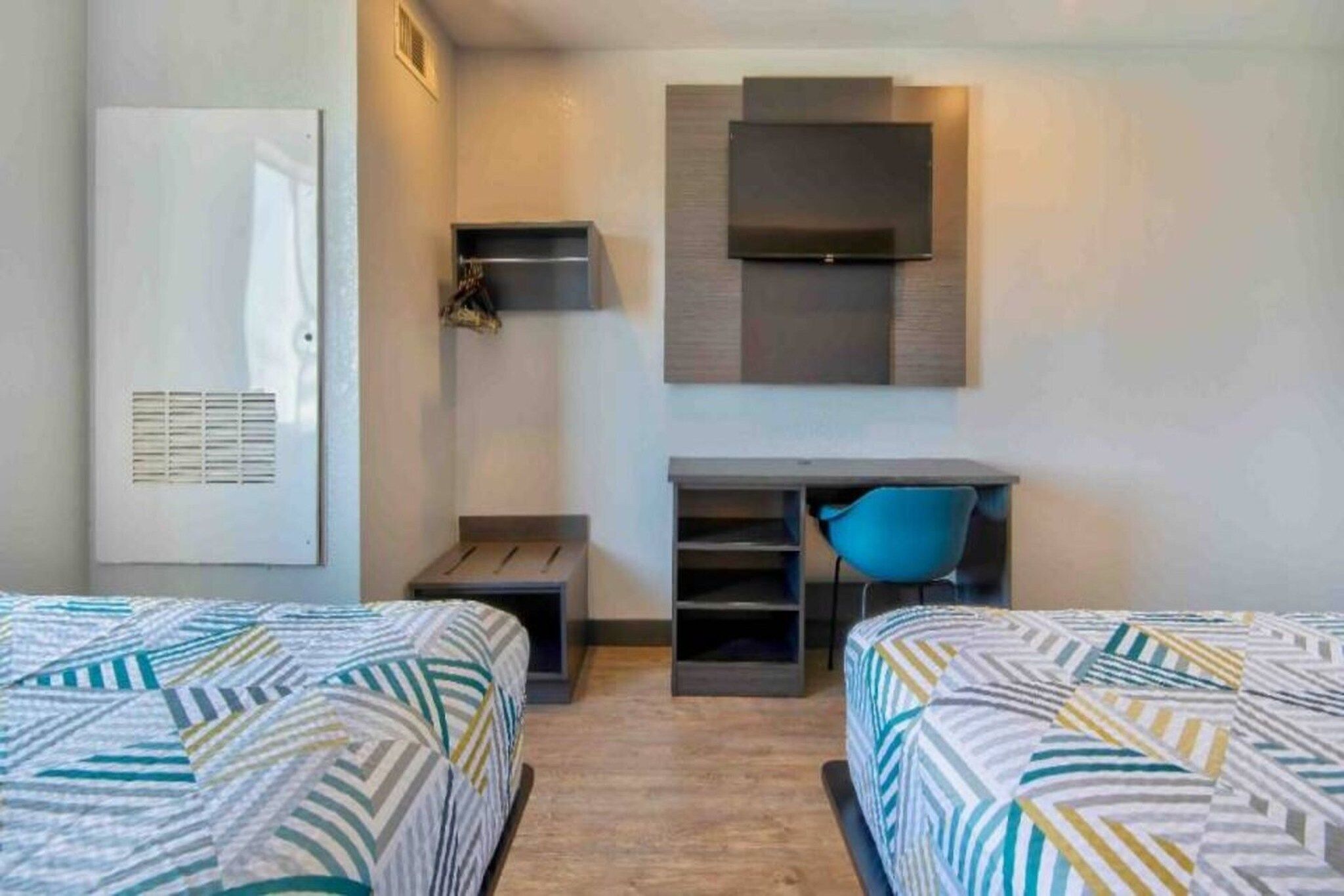 A hotel room with two beds, a desk, a chair, and a TV.