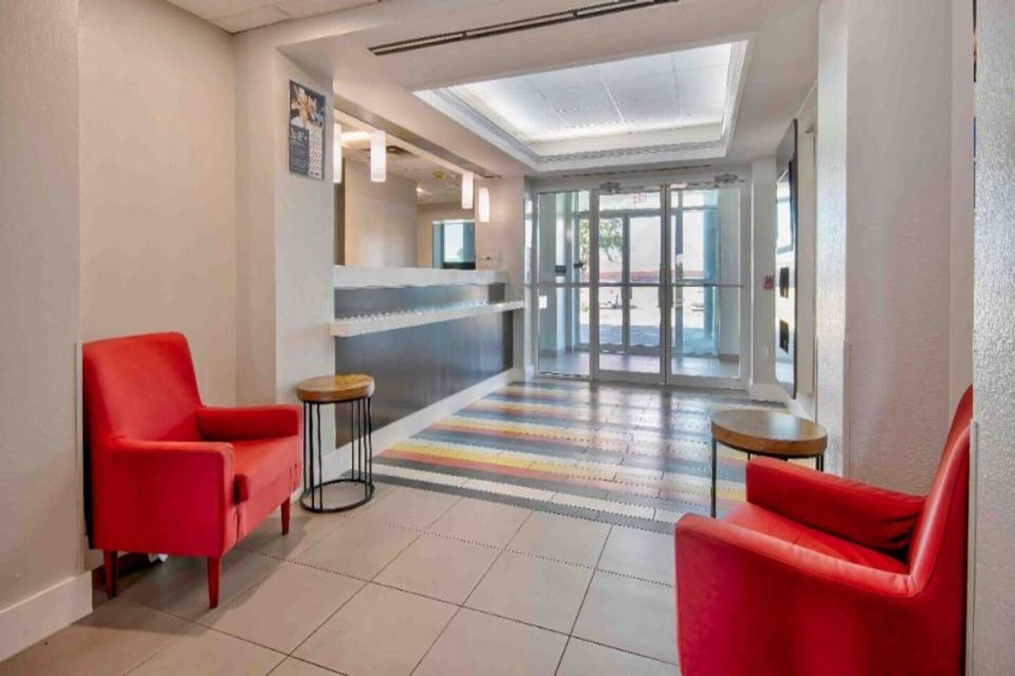 A hotel lobby with red chairs, a reception desk, and a colorful striped carpet.