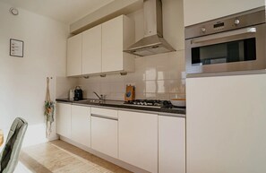 A kitchen with white cabinets, a stainless steel range hood, and a built-in oven. - Sea-view apartment Sea Bass in Egmond aan Zee for 4 guests, with 2 bedrooms and two sunny terraces. (Egmond aan Zee)