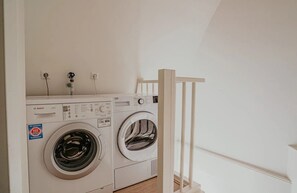 A laundry area with two washing machines, a wooden railing, and a white wall. - Sea-view apartment Sea Bass in Egmond aan Zee for 4 guests, with 2 bedrooms and two sunny terraces. (Egmond aan Zee)
