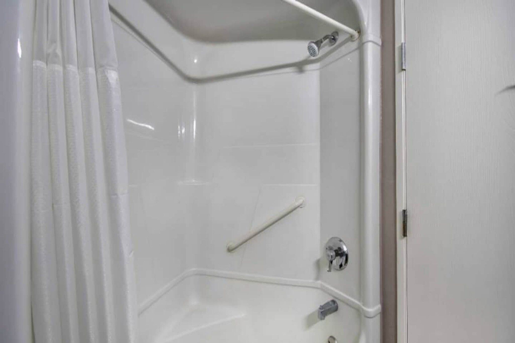 A corner shower with a white door, a shower curtain, and a grab bar.