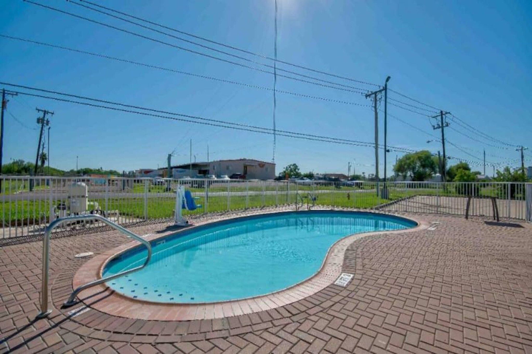A swimming pool with a brick deck, surrounded by a fence, and utility poles in the background.
