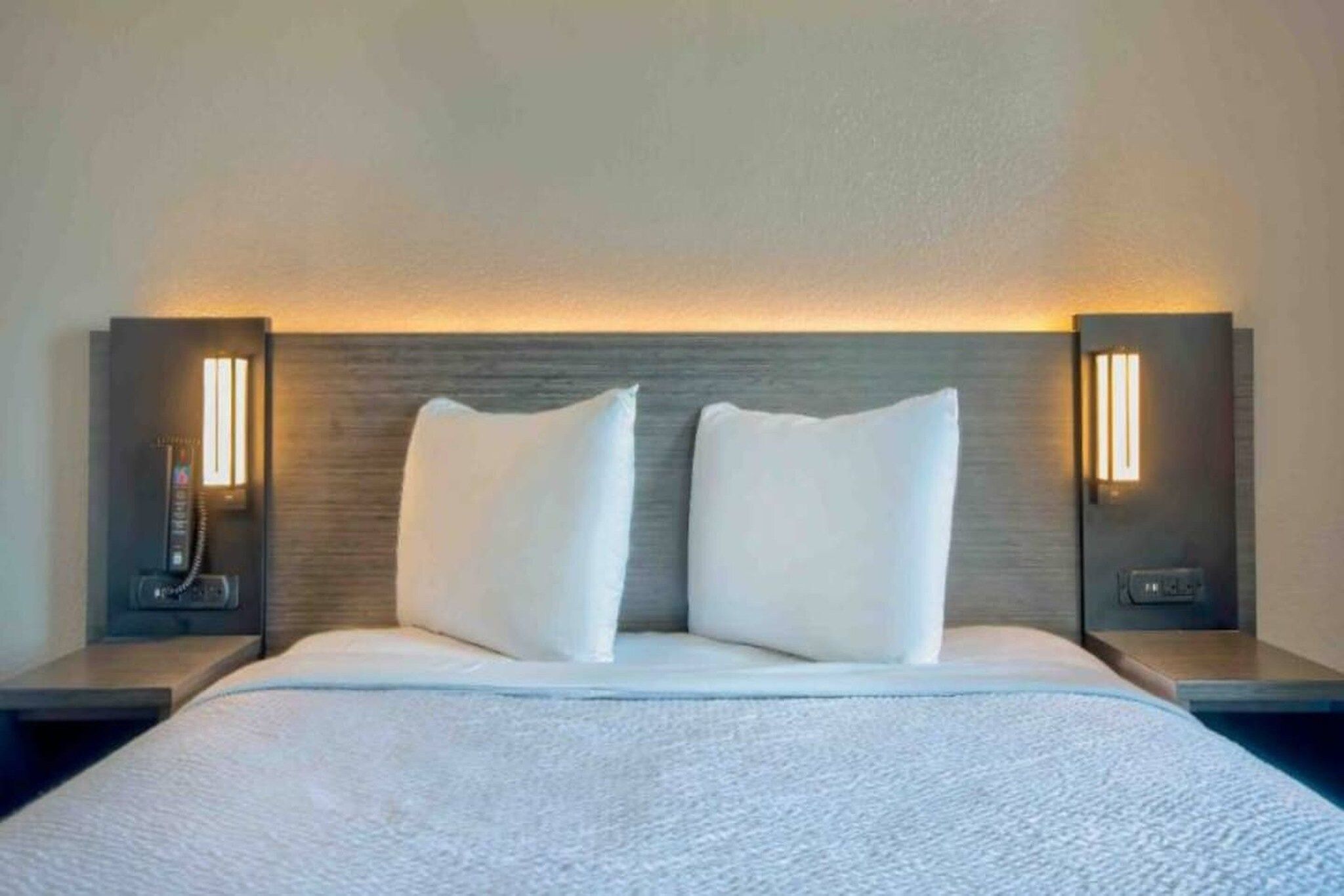 A hotel room with a large bed, two white pillows, and two bedside tables with lamps.