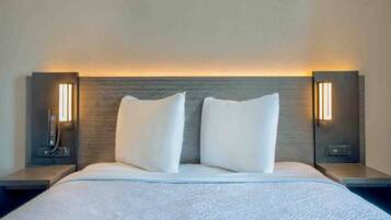 A hotel room with a large bed, two white pillows, and two bedside tables with lamps.