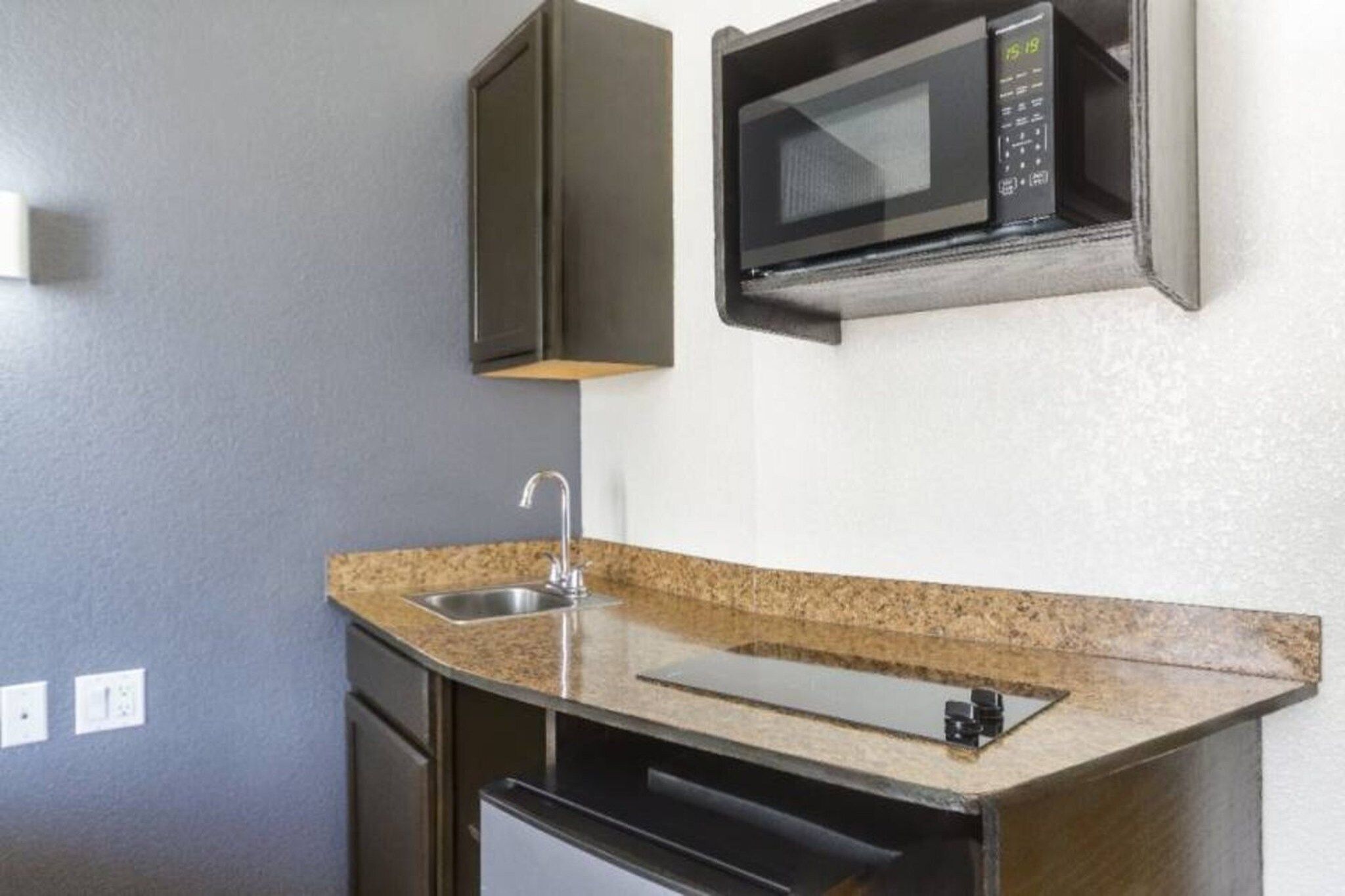 Una cocina compacta con microondas integrado, pileta de acero inoxidable y encimera de granito.