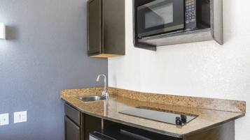Una cocina compacta con microondas integrado, pileta de acero inoxidable y encimera de granito.
