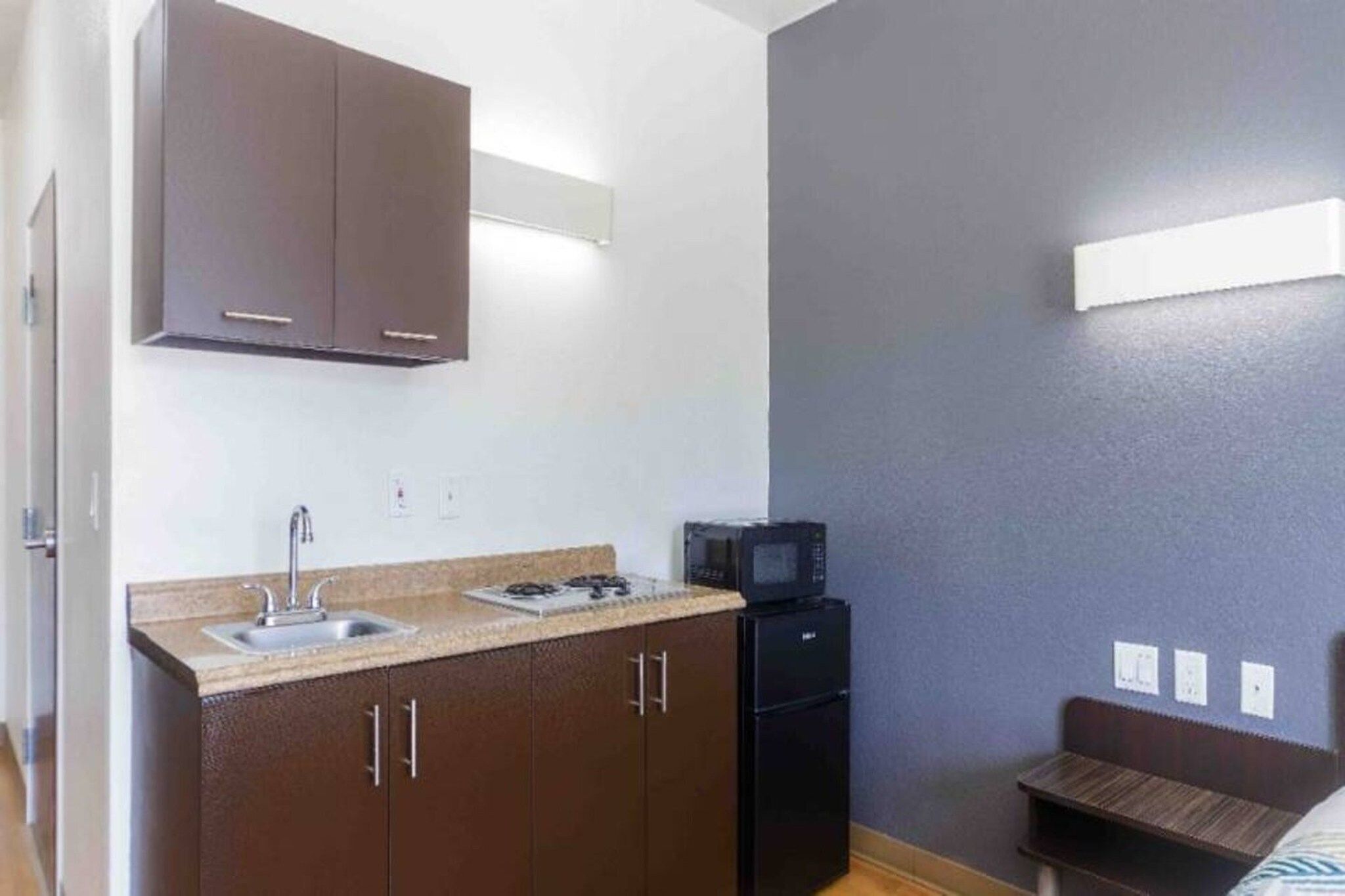 Una kitchenette compacta con un lavamanos, estufa y microondas, además de una pequeña mesa de comedor.