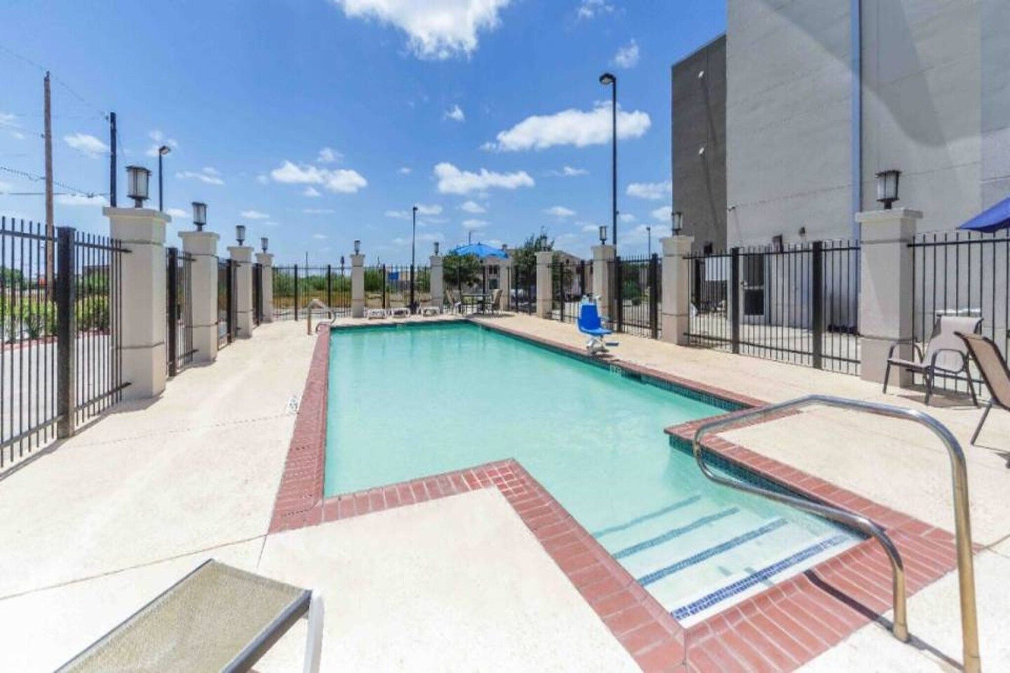Piscina rectangular con borde de azulejos, rodeada por una valla, y un cielo despejado arriba.